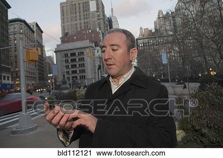 Stock Image - Hispanic businessman using cell phone on city street. Fotosearch