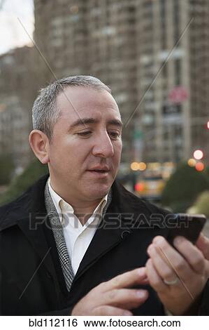 Stock Photograph - Hispanic businessman using cell phone on city street. Fotosearch