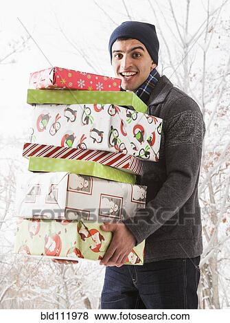 Hispanic man holding Christmas gifts in snow View Large Photo Image Stock Photo - Hispanic man holding Christmas gifts in snow. Fotosearch