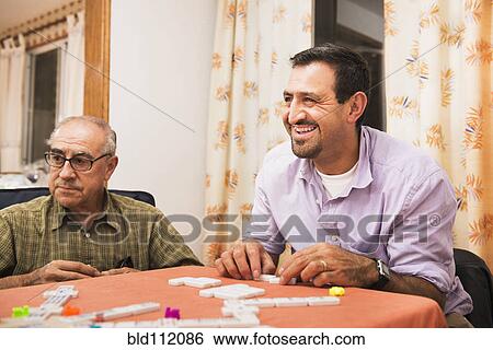 Stock Photograph - Hispanic men playing dominoes at table. Fotosearch
