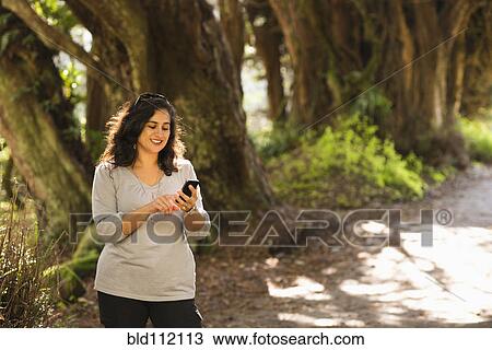 Stock Image - Hispanic woman using cell phone outdoors. Fotosearch