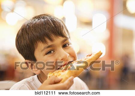 Stock Image - Mixed race boy eating pizza in restaurant. Fotosearch