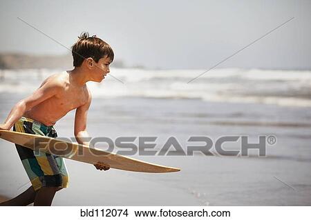 Picture - Mixed race boy holding board on beach. Fotosearch