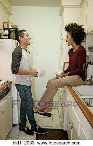Stock Image - Mixed race couple relaxing in kitchen. Fotosearch