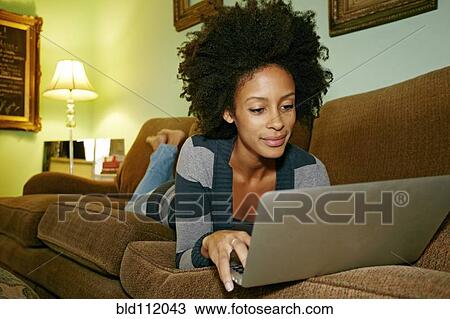 Stock Image - Mixed race woman using laptop on sofa. Fotosearch