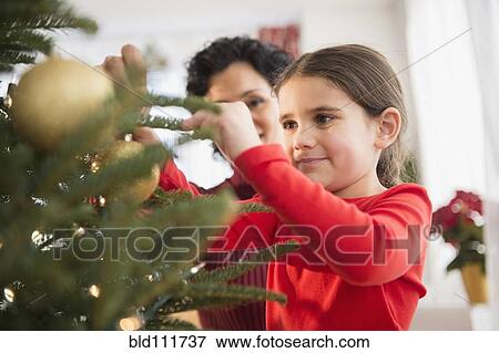 Stock Photo - Mother and daughter decorating Christmas tree. Fotosearch