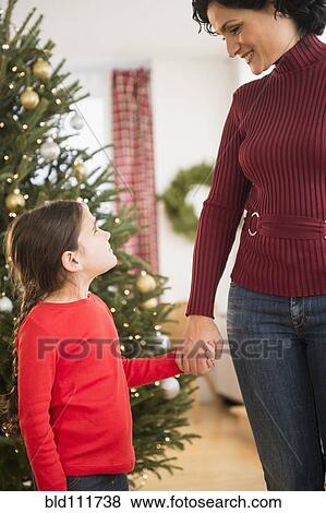 Stock Photo - Mother and daughter holding hands by Christmas tree. Fotosearch
