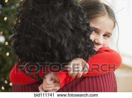 Stock Image - Mother and daughter hugging by Christmas tree. Fotosearch