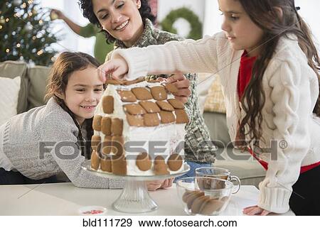 Stock Photo - Mother and daughters making gingerbread house. Fotosearch
