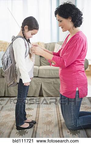 Stock Image - Mother buttoning daughter's sweater in living room. Fotosearch