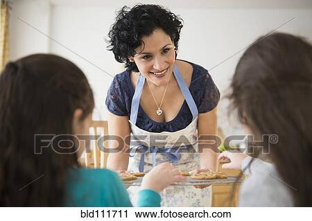 Stock Image - Mother giving daughters fresh baked cookies. Fotosearch