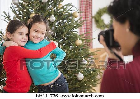 Mother taking picture of daughters by Christmas tree View Large Photo Image Stock Photograph - Mother taking picture of daughters by Christmas tree. Fotosearch