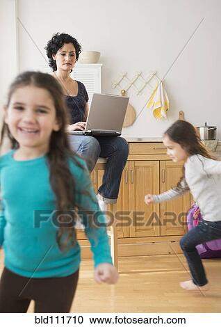 Stock Image - Mother using laptop as daughters play. Fotosearch
