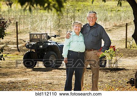 Stock Image - Older Caucasian couple smiling in olive grove. Fotosearch