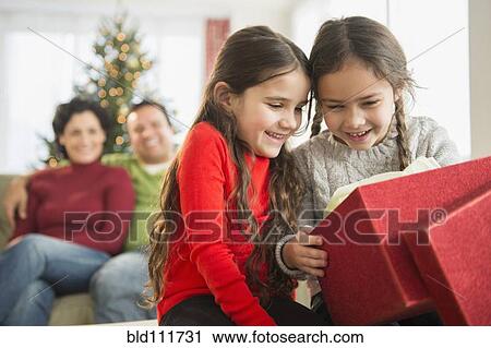 Stock Image - Smiling girls opening Christmas present. Fotosearch