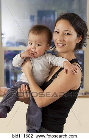 Smiling Korean mother holding baby View Large Photo Image Stock Image - Smiling Korean mother holding baby. Fotosearch