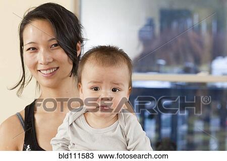 Stock Image - Smiling Korean mother holding baby. Fotosearch