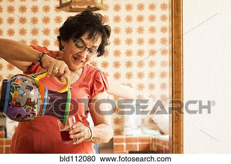 Stock Image - Woman pouring glass of juice in kitchen. Fotosearch