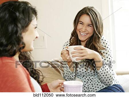 Stock Image - Women having coffee together on sofa. Fotosearch