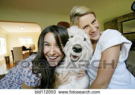 Stock Image - Women petting dog in kitchen. Fotosearch