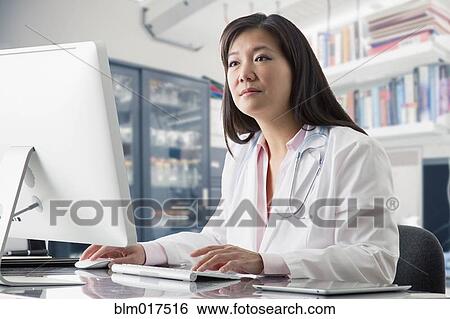 Stock Photograph - Asian doctor working at computer in hospital. Fotosearch