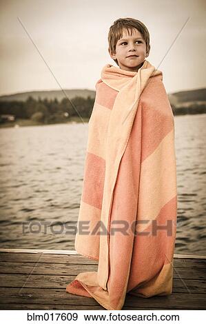 Stock Photo - Caucasian boy wrapped in towel on wooden dock. Fotosearch