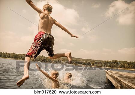 Stock Image - Caucasian boys jumping off wooden dock. Fotosearch