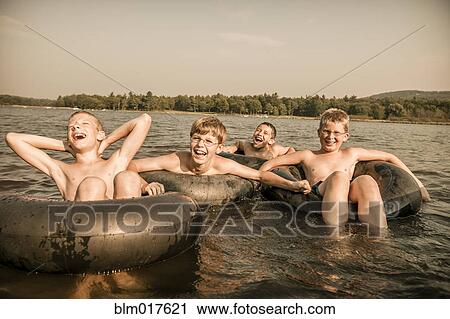 Stock Image - Caucasian boys with inner tubes in water. Fotosearch