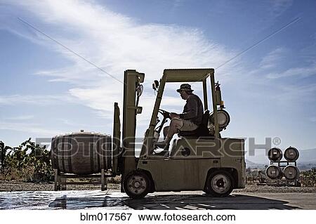 Stock Photo - Caucasian farmer driving forklift with barrel. Fotosearch
