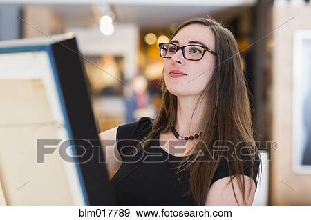 Stock Photo - Caucasian woman examining painting in art gallery. Fotosearch