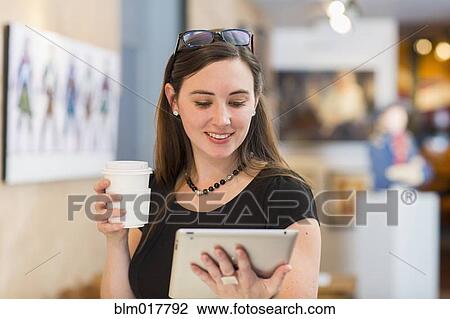 Stock Image - Caucasian woman using tablet computer in art gallery. Fotosearch