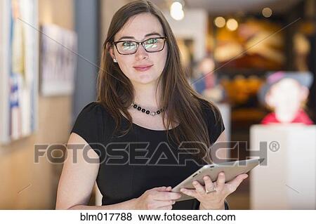 Stock Photo - Caucasian woman using tablet computer in art gallery. Fotosearch