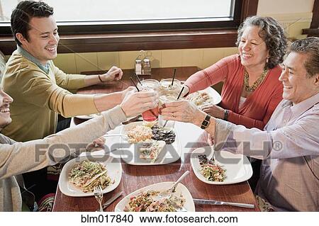Stock Image - Hispanic family toasting each other at restaurant. Fotosearch