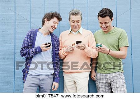 Stock Photo - Hispanic father and sons using cell phones outdoors. Fotosearch