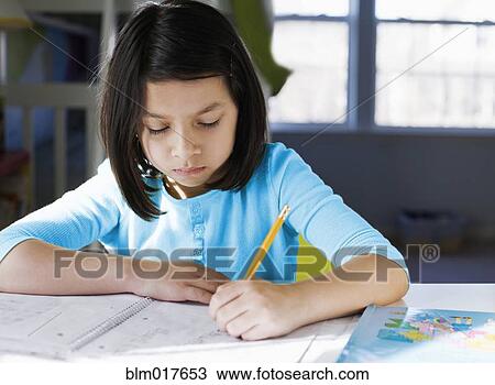 Stock Image - Hispanic girl doing homework at desk. Fotosearch