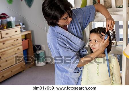 Stock Photo - Hispanic mother brushing daughter's hair. Fotosearch