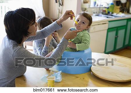 Hispanic mother feeding toddler in high chair View Large Photo Image Stock Image - Hispanic mother feeding toddler in high chair. Fotosearch