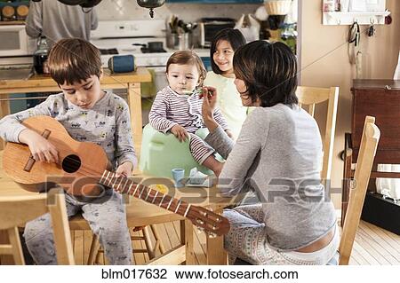 Stock Image - Hispanic mother feeding toddler in kitchen. Fotosearch