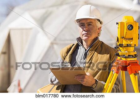 Stock Image - Hispanic surveyor working outdoors. Fotosearch