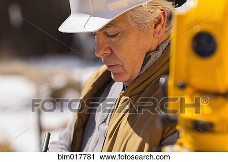 Stock Image - Hispanic surveyor working outdoors. Fotosearch