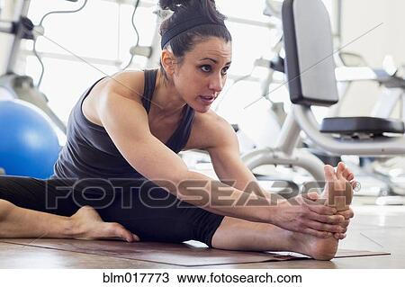 Stock Image - Hispanic woman stretching in gym. Fotosearch