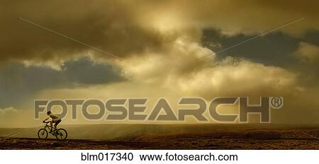 Stock Image - Man riding bicycle on dirt road. Fotosearch