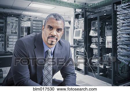 Stock Image - Mixed race businessman sitting in server room. Fotosearch