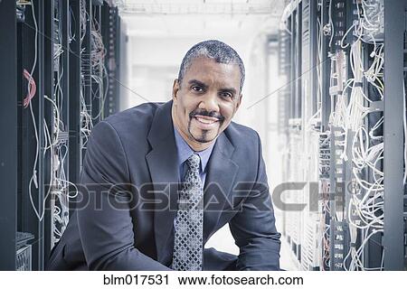 Stock Image - Mixed race businessman sitting in server room. Fotosearch