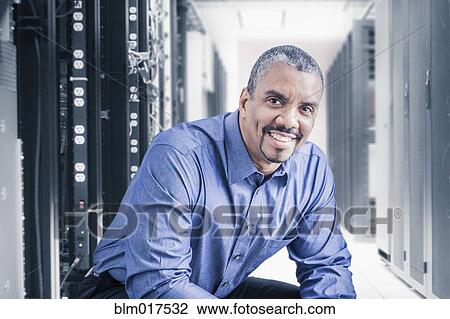 Stock Image - Mixed race businessman sitting in server room. Fotosearch