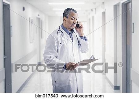 Stock Image - Mixed race doctor talking on cell phone in hospital. Fotosearch