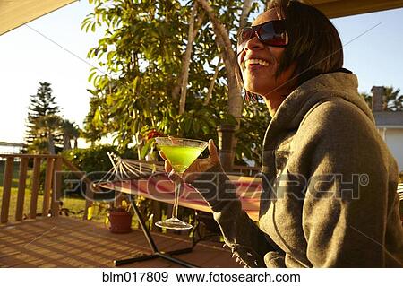 Stock Photo - Mixed race woman having cocktail on porch. Fotosearch