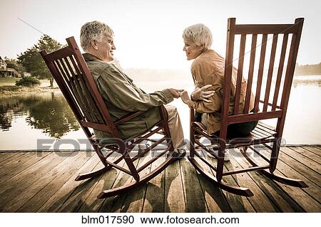 Stock Image - Older Caucasian couple sitting on wooden dock. Fotosearch