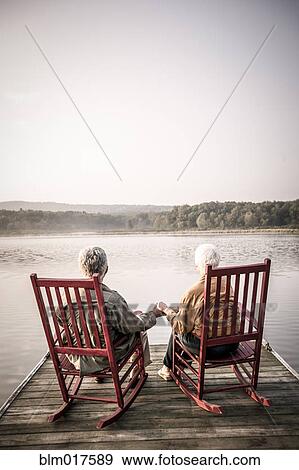 Stock Photo - Older Caucasian couple sitting on wooden dock. Fotosearch