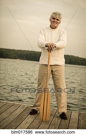 Stock Photograph - Older Caucasian man holding oar on wooden dock. Fotosearch